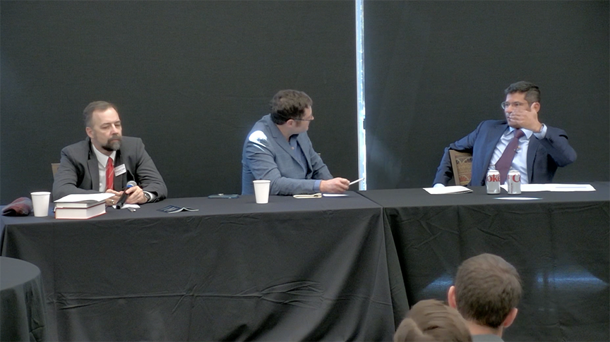 Panelists, three men in suits at a table